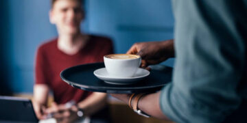 Unrecognizable African-American barista bringing an order to customer in a cafeteria